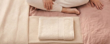 bedroom scene with warm light, rumpled bedding, and a folded towel, suggesting a surprising but normal body response during sex or masturbation