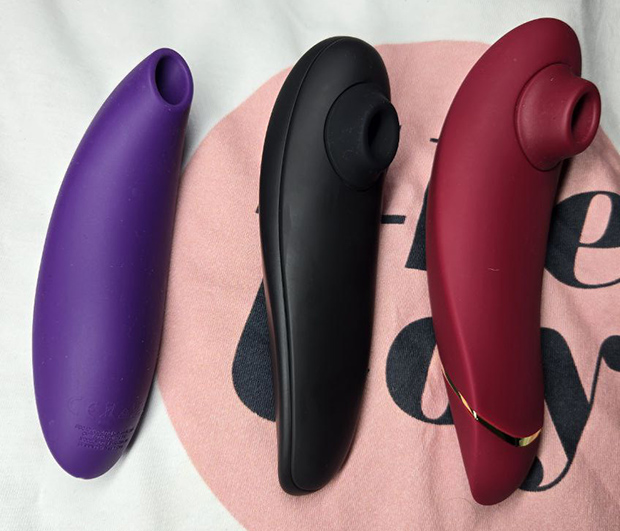 Side-by-side photo of three suction toys—Melt 2 (purple), Womanizer Classic 2 (black), and Womanizer Premium 2 (red)—on a “The Toy” background, showing differences in size, nozzle depth, and body shape from personal collection.