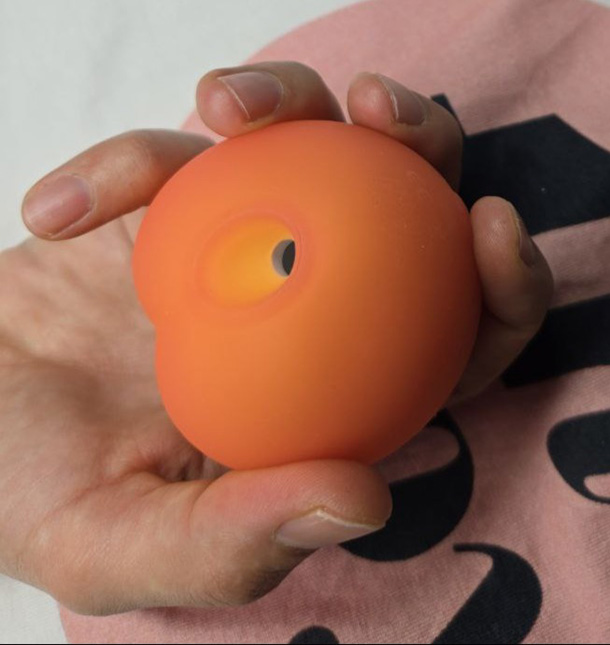 Hand holding Womanizer Peach toy demonstrating natural grip position with thumb near control buttons