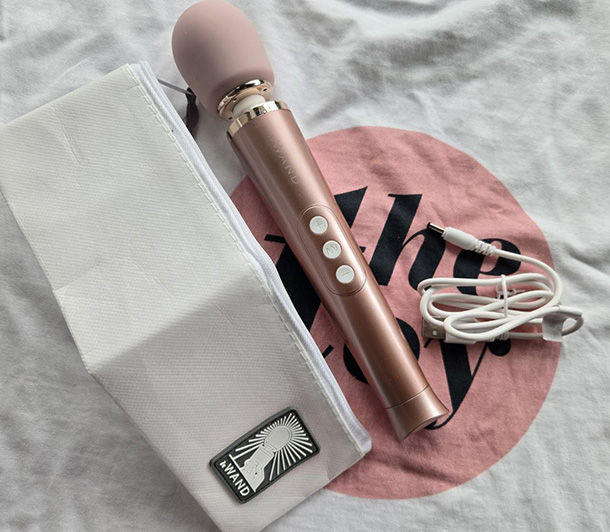 Le Wand Petite vibrator in rose gold displayed alongside its USB charging cable, travel bag, user guide, and pleasure guide