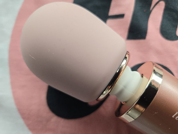 Close-up of the Le Wand Petite's round silicone head in light pink, showing the firmer Shore A 48 material against a fingertip pressing into it