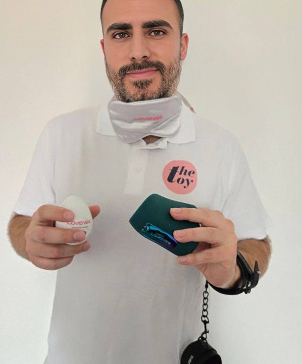Michael holding the Lovense Hush 2 in one hand and the Kraken masturbator in the other. The blindfold from the set under his chin and demonstrating the handcuffs.