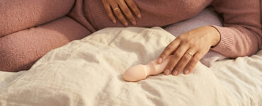 photo of a person resting with a vibrator in warm light, suggesting calm experimentation with layered touch rather than intense stimulation.