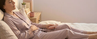 Soft editorial photo of a person alone on a bed in warm light, suggesting a shift from sensual exploration into self-monitoring during masturbation.