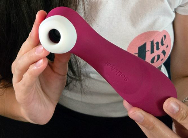 Hand holding the Satisfyer Pro 2 Generation 3 showing the ergonomic tapered handle, matte silicone texture, and three ridged control buttons on the back of the toy