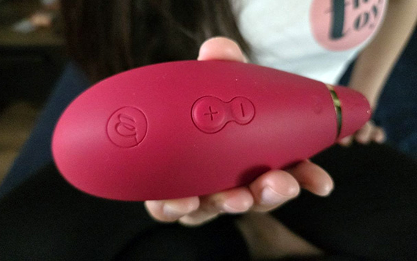Close-up of the Womanizer Premium 2's four control buttons: power on/off at the bottom, Autopilot in the middle, and plus/minus intensity buttons at the top, all in matching Raspberry pink.