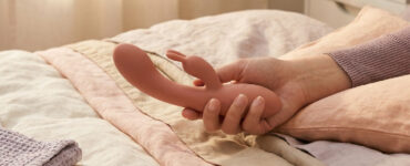 close-up of a relaxed hand holding a vibrator on neutral bedding, suggesting comfortable grip, support, and easier solo play.