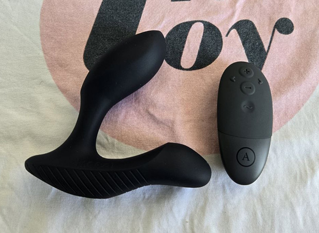 Arcwave Perk wireless remote control placed next to the prostate massager, showing the plus, minus, and arrow buttons used for adjusting vibration patterns and intensity