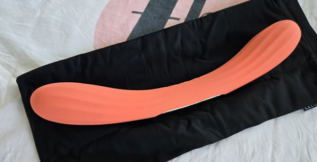 The LELO Boomerang double-ended vibrator in coral orange displayed alongside its satin storage pouch