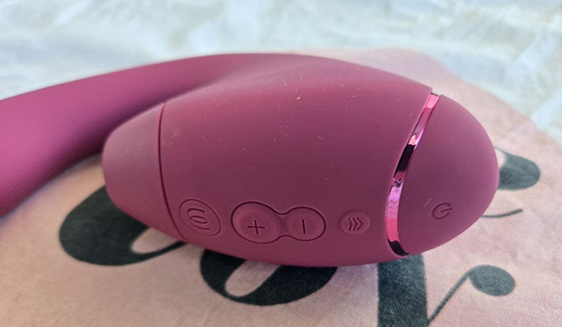 Front control panel of the Womanizer Next Duo showing three buttons: a larger textured plus button for Pleasure Air intensity, a smaller minus button, and the Climax Control button with directional arrows.